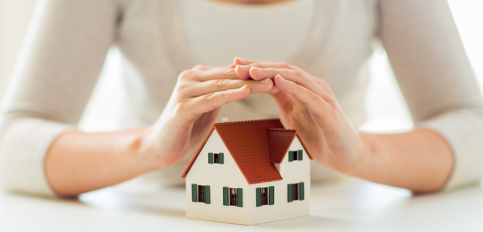 architecture, safety, security, real estate and property concept - close up of hands protecting house or home model